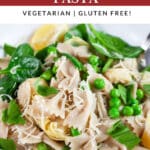 Spring vegetable pasta in white bowl with fork garnished with Parmesan cheese, lemon wedges, and fresh basil.