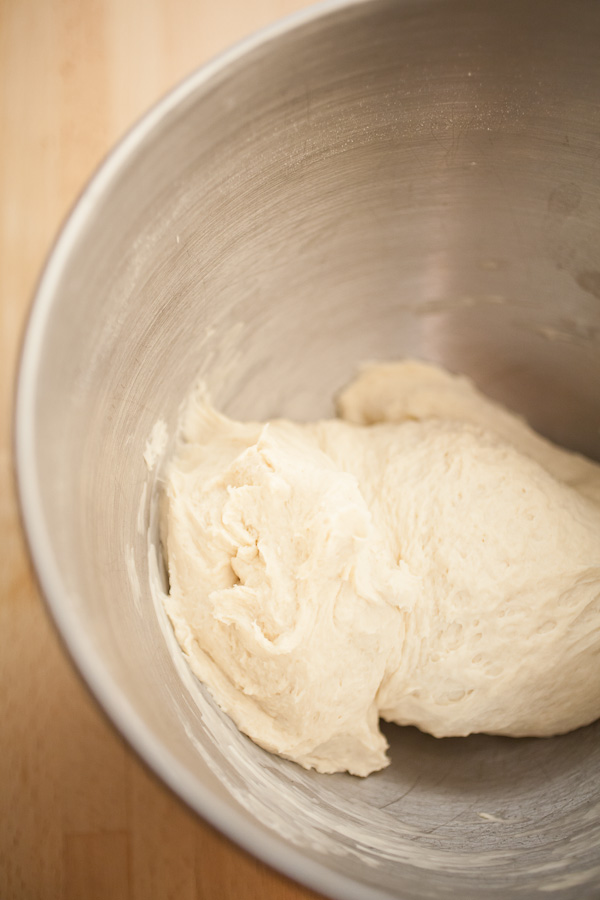 Wet pizza dough in metal bowl.