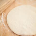 Homemade pizza dough with wooden rolling pin.