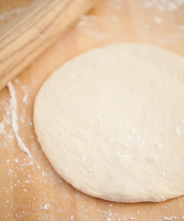 Homemade pizza dough with wooden rolling pin.