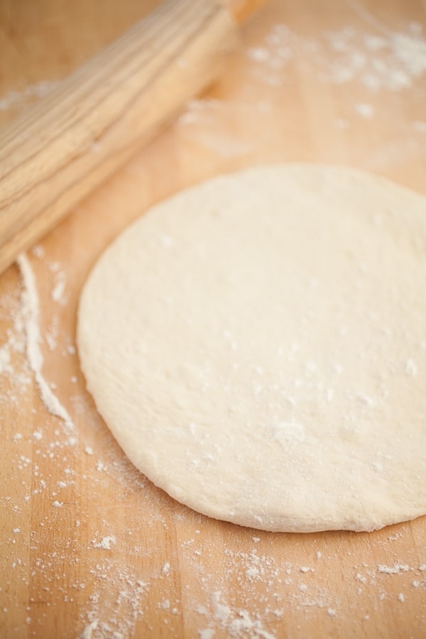 Homemade pizza dough with wooden rolling pin.