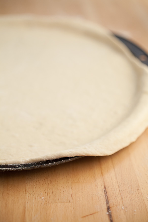 Learn How To Make Homemade Pizza Dough! This simple pizza dough recipe makes the best pizza crusts. This rustic homemade dough is easy and has tons of uses! Make a thin crust or deep dish pizza or an Italian calzone. You can make it in a Kitchen Aid mixer or knead it by hand. There's nothing like a homemade pizza dough for healthy dinners! #pizza #pizzadough #howtomake #homemade #pizzacrust Rolled out pizza dough on metal pizza pan.
