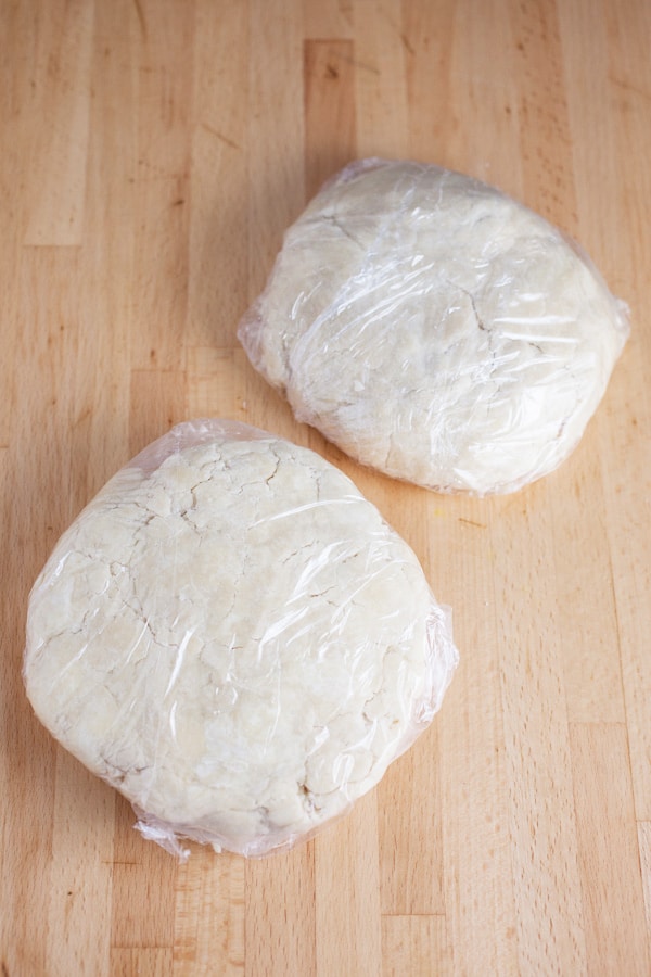 Two balls of pie dough wrapped in plastic wrap.
