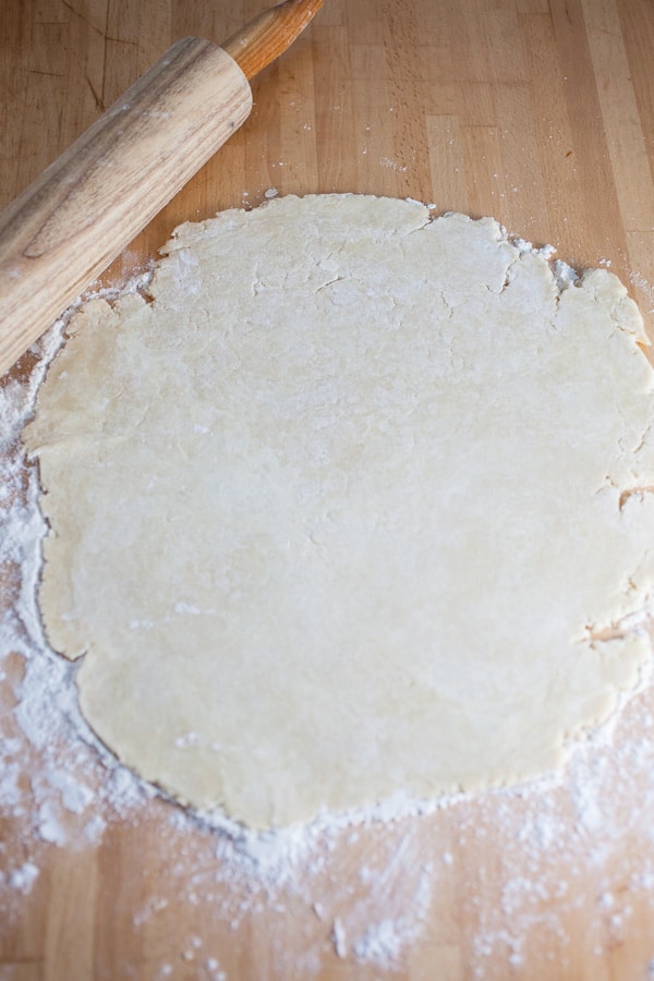 Pie dough rolled out next to wooden rolling pin.