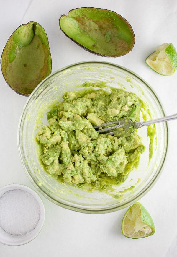 Guacamole in small glass bowl with avocadoes and limes.