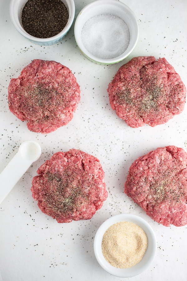 Raw spiced ground beef patties on white surface.