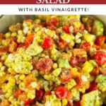Tomato corn avocado salad with basil vinaigrette in ceramic bowl with spoon.