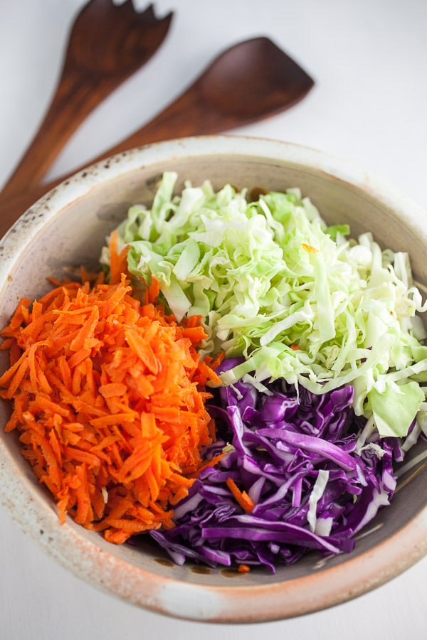 Shredded red and green cabbage and grated carrots in ceramic bowl.