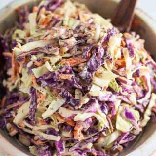 Red and green cabbage coleslaw in ceramic bowl with wooden spoon.