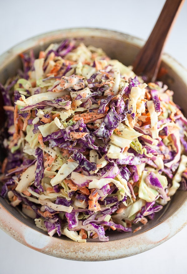 Red and green cabbage coleslaw in ceramic bowl with wooden spoon.