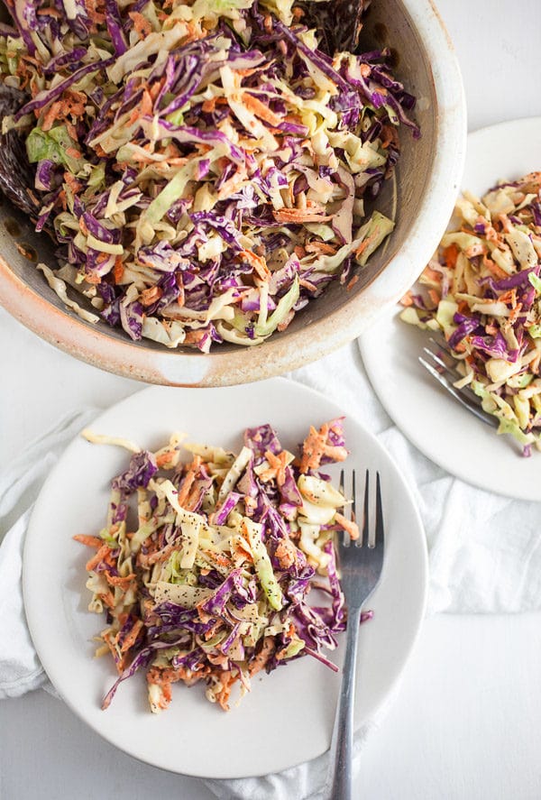 Red and green cabbage coleslaw on small white plates and in ceramic bowl.