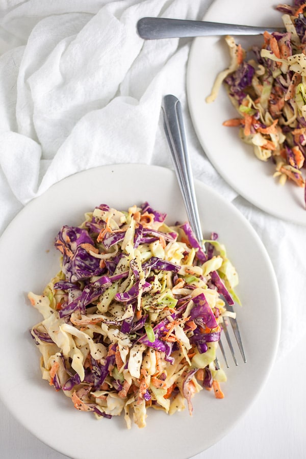 Red and green cabbage coleslaw on small white plates with forks.