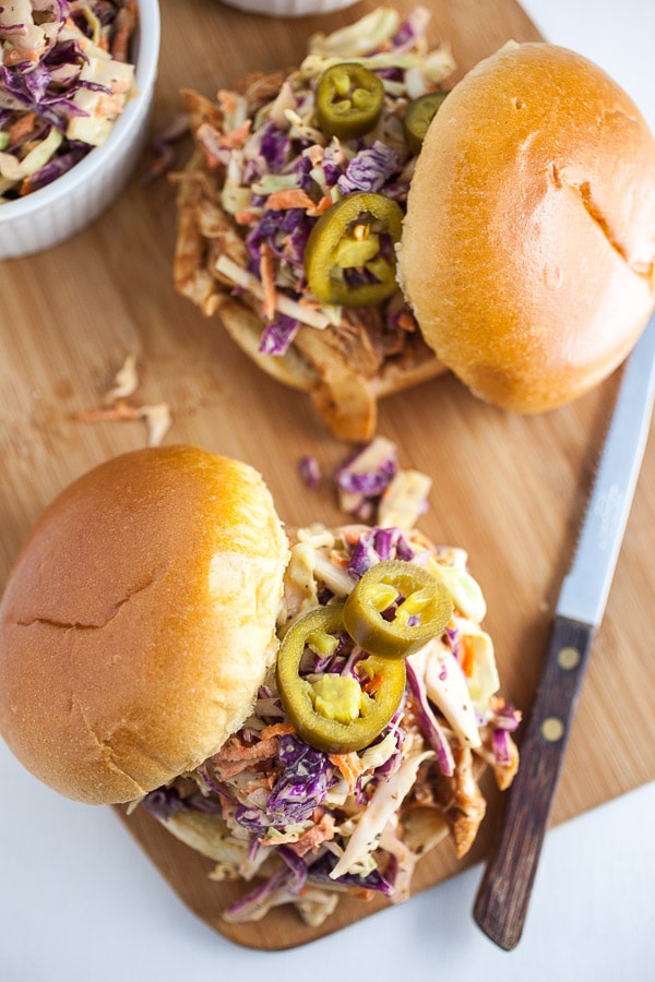 BBQ chicken sandwiches with slaw and jalapenos on wooden cutting board.