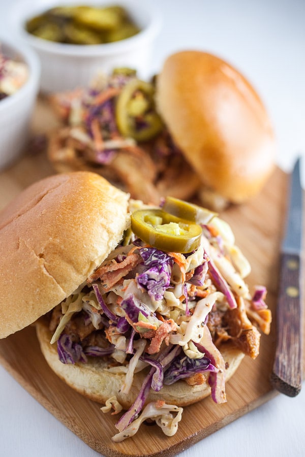 Slow cooker BBQ chicken sandwiches on buns with slaw on wooden cutting board.