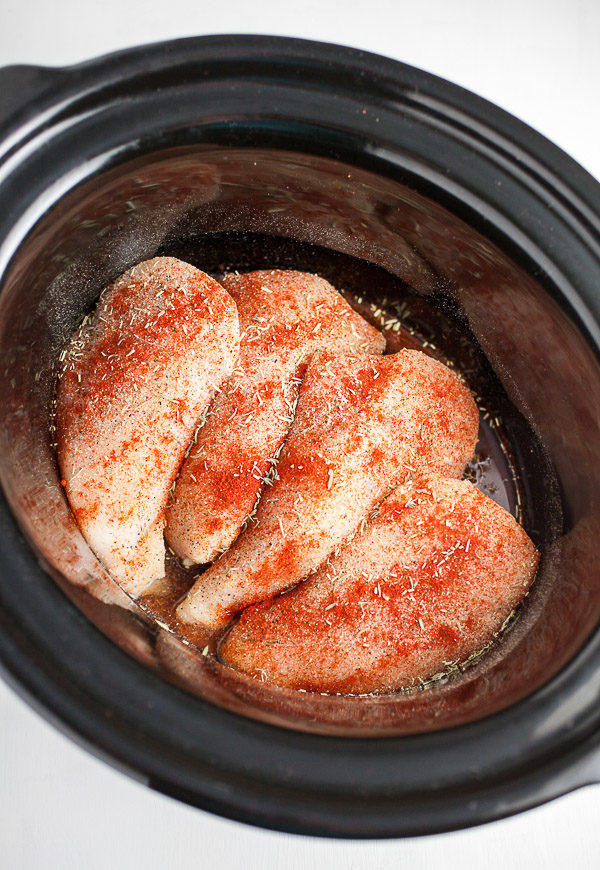 Raw chicken breasts and spices in slow cooker.