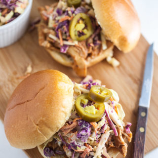 Slow cooker BBQ chicken sandwiches with coleslaw on buns on wooden cutting board.