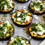 Grilled eggplant with feta and fresh herbs on baking sheet.