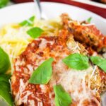 Baked eggplant Parmesan garnished with fresh basil with spaghetti in bowl with fork.