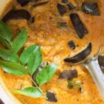 South Indian eggplant curry in Dutch oven with metal spoon.
