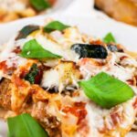 Slice of garden vegetable lasagna garnished with fresh basil on white plate.