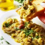 Greek eggplant dip on bread lifted from white serving platter.