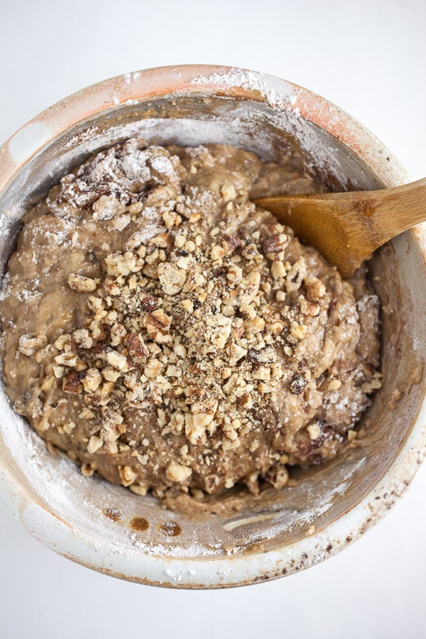 Banana muffin batter with walnuts in ceramic bowl with wooden spoon.