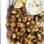 Diced roasted eggplant in white dish with white sauce and lemon wedges.
