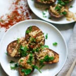 Roasted baby eggplants with tahini and za'atar garnished with fresh herbs on white plates.