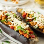 Stuffed eggplant with chicken and mozzarella cheese on white platter with fork.