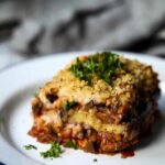 Vegan eggplant lasagna on white plate garnished with fresh parsley.
