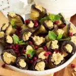 Georgian eggplant walnut rolls in white serving bowl garnished with pomegranate arils and fresh mint.