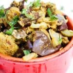 Indian spiced stuffed eggplant and potatoes in red serving bowl.