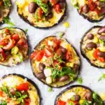 Grilled eggplant tacos on white surface garnished with fresh cilantro.