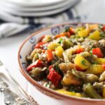 Mediterranean roasted eggplant salad in bowl next to silverware and stack of white plates.