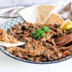 Zaalouk Moroccan eggplant tomato dip on serving platter with flatbread and fresh herbs.
