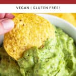 Poblano avocado dip on tortilla chip lifted from white bowl.