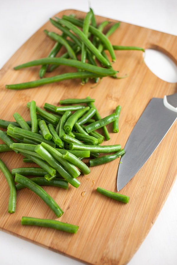 Chopped green beans on wooden cutting board with knife.