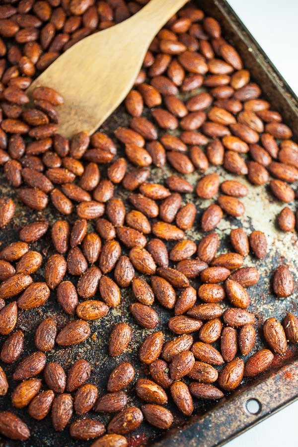 Roasted toasted almonds on metal baking sheet with wooden spatula.