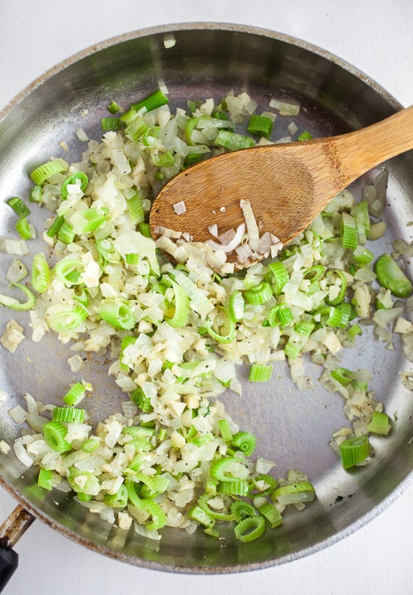 Garlic, onions, and fennel sautéed in skillet with wooden spoon. 