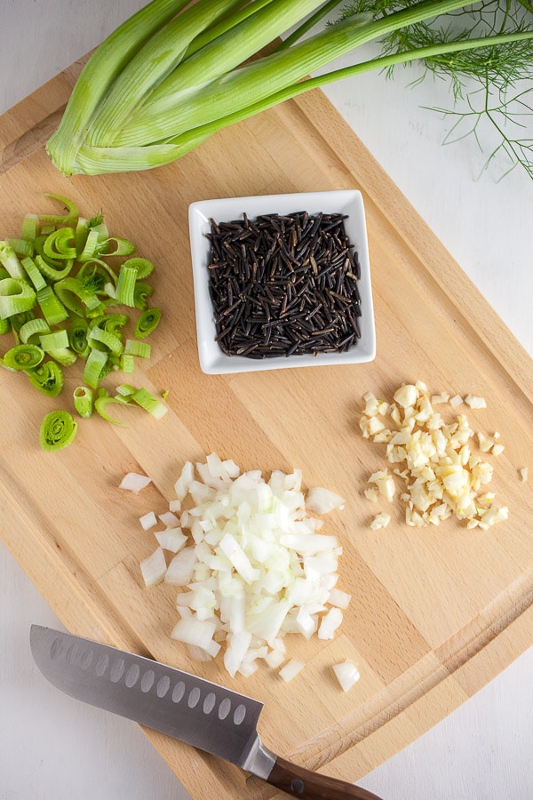 Minced garlic, onions, fennel, and wild rice on wooden cutting board.