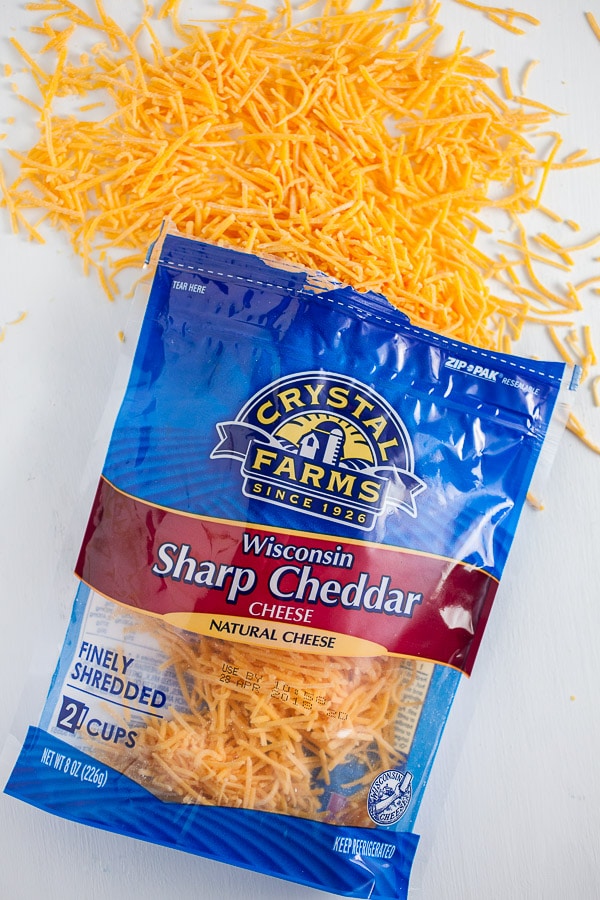 Shredded cheddar cheese spilling from package on white surface.