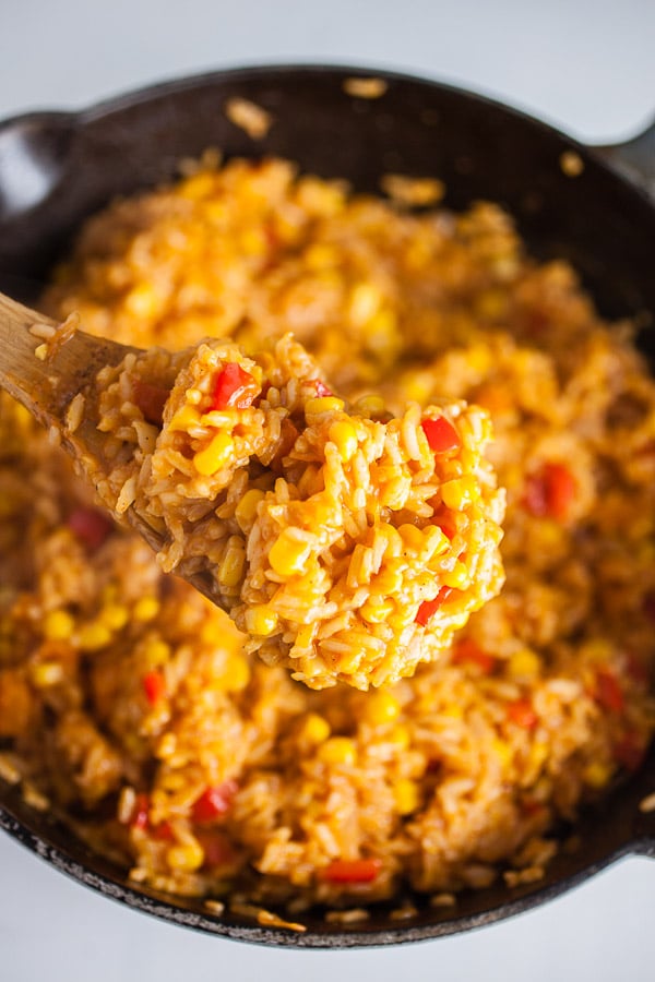 Scoop of cooked cheesy Spanish rice lifted from cast iron Dutch oven on wooden spoon.