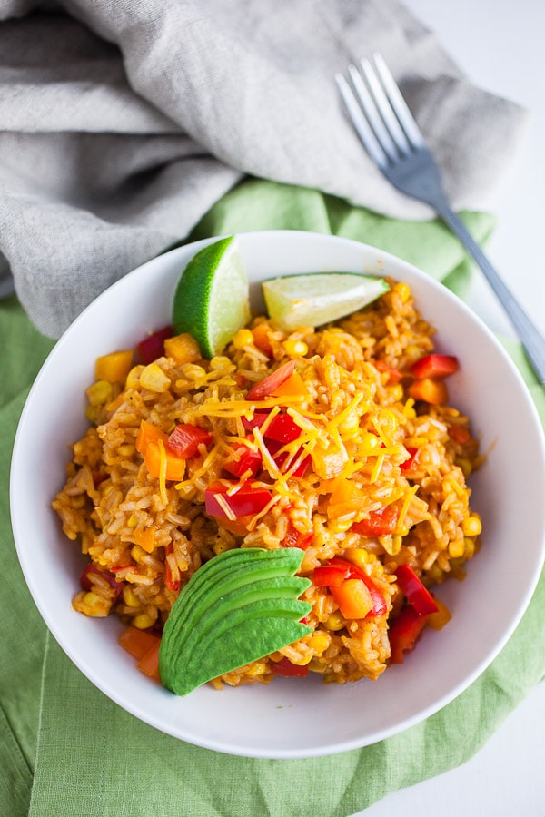 Cheesy Spanish rice with sliced avocado and lime wedges in white bowl.