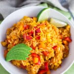 Cheesy Spanish rice with sliced avocado and lime wedges in white bowl.