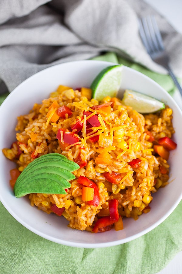 Cheesy Spanish rice with sliced avocado and lime wedges in white bowl.