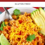Cheesy Spanish rice in white bowl with fork garnished with fresh cilantro, avocado, and lime.