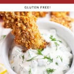 Breaded fish finger dipped into small white bowl of dill tartar sauce.