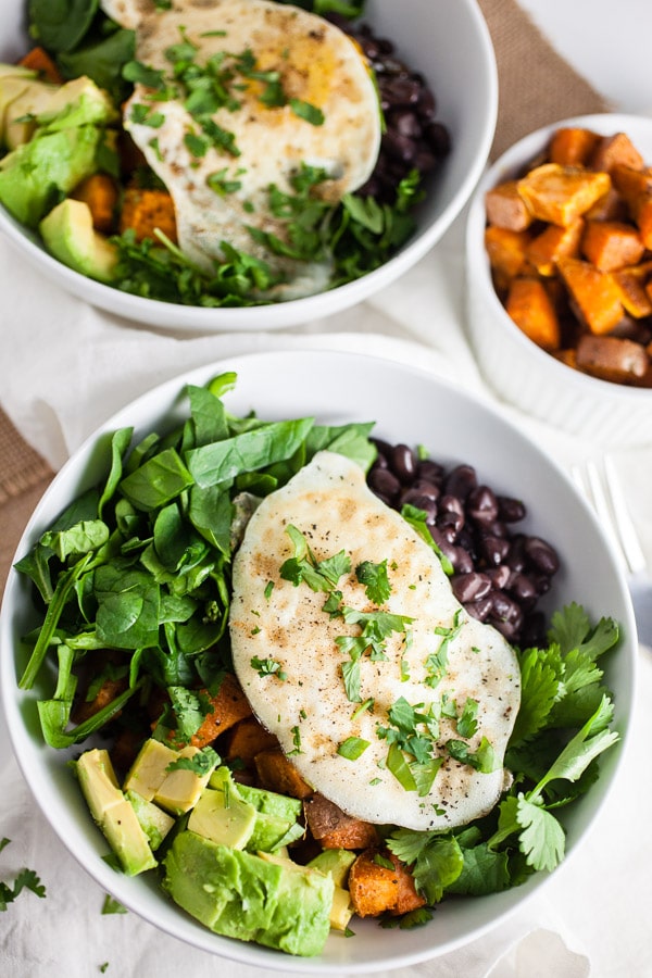 Breakfast bowls with sweet potatoes, black beans, spinach, avocado, egg, and cilantro in white bowls.