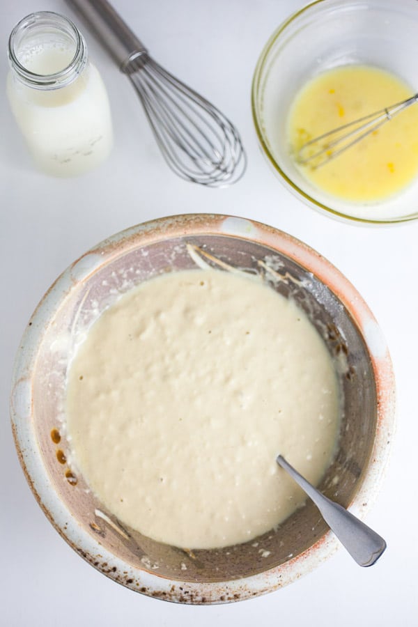 Pancake batter in ceramic mixing bowl next to glass jar of milk.