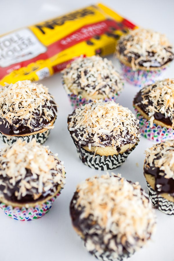 Toasted coconut chocolate chip cupcakes on white surface next to bag of chocolate chips.